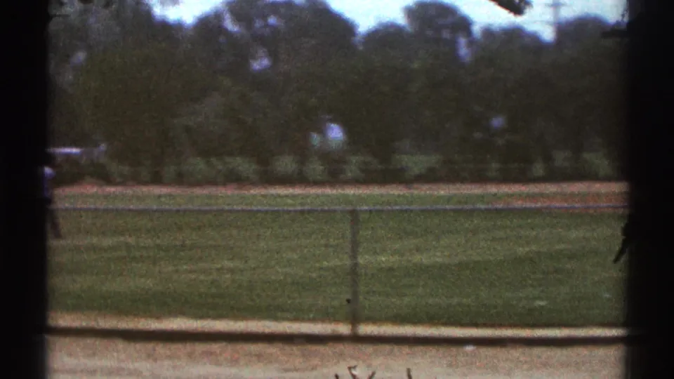 Fenced public field in Woodland Hills, California, seen from a shaded spectator position during a 1969 home-movie baseball scene.