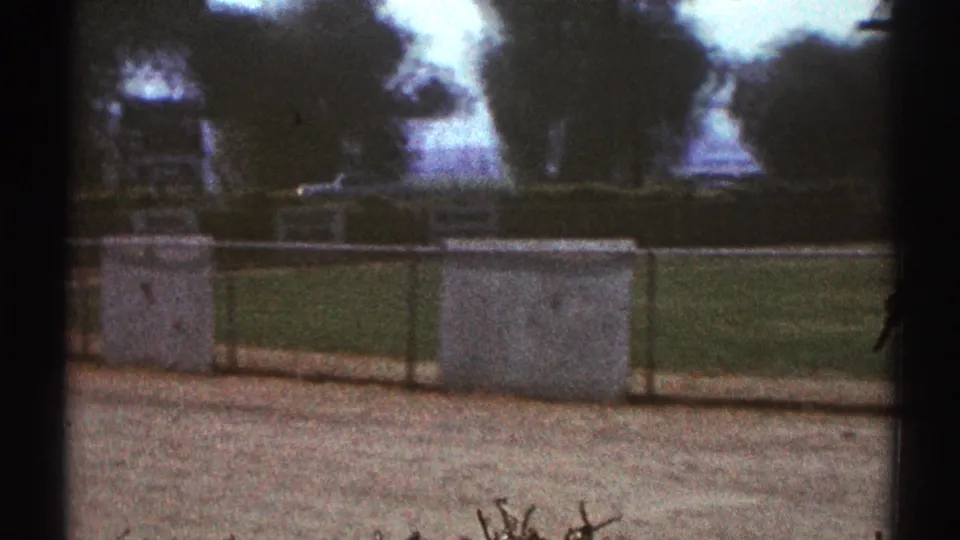 Woodland Hills public field view with concrete structures, chain-link fencing, grass, and trees captured on faded 8mm film.