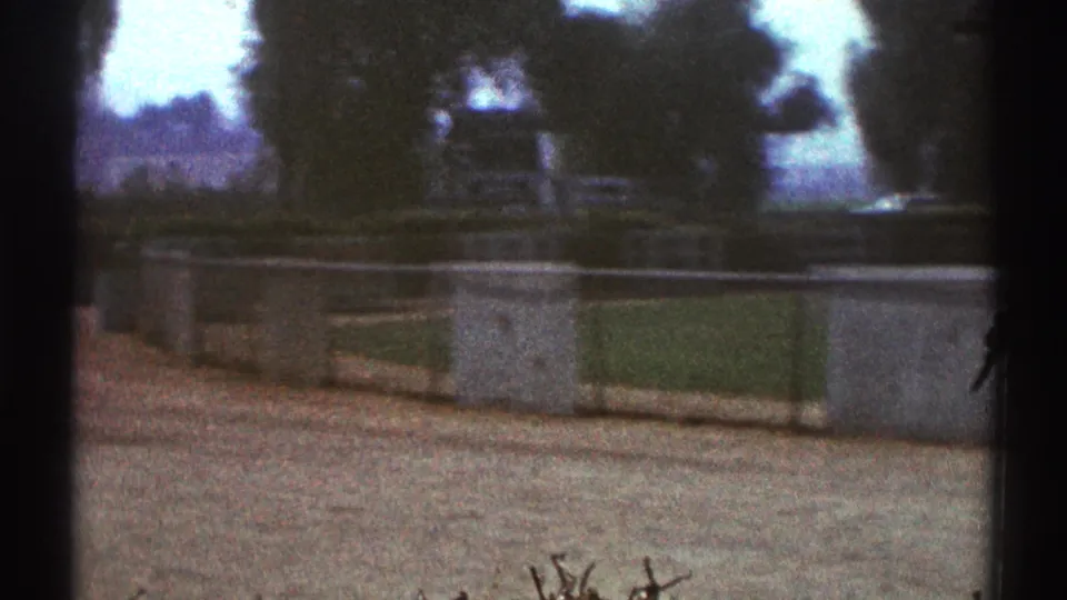 1969 Woodland Hills home-movie frame with pavement, trees, low barriers, and dark vertical edges from the filming position.