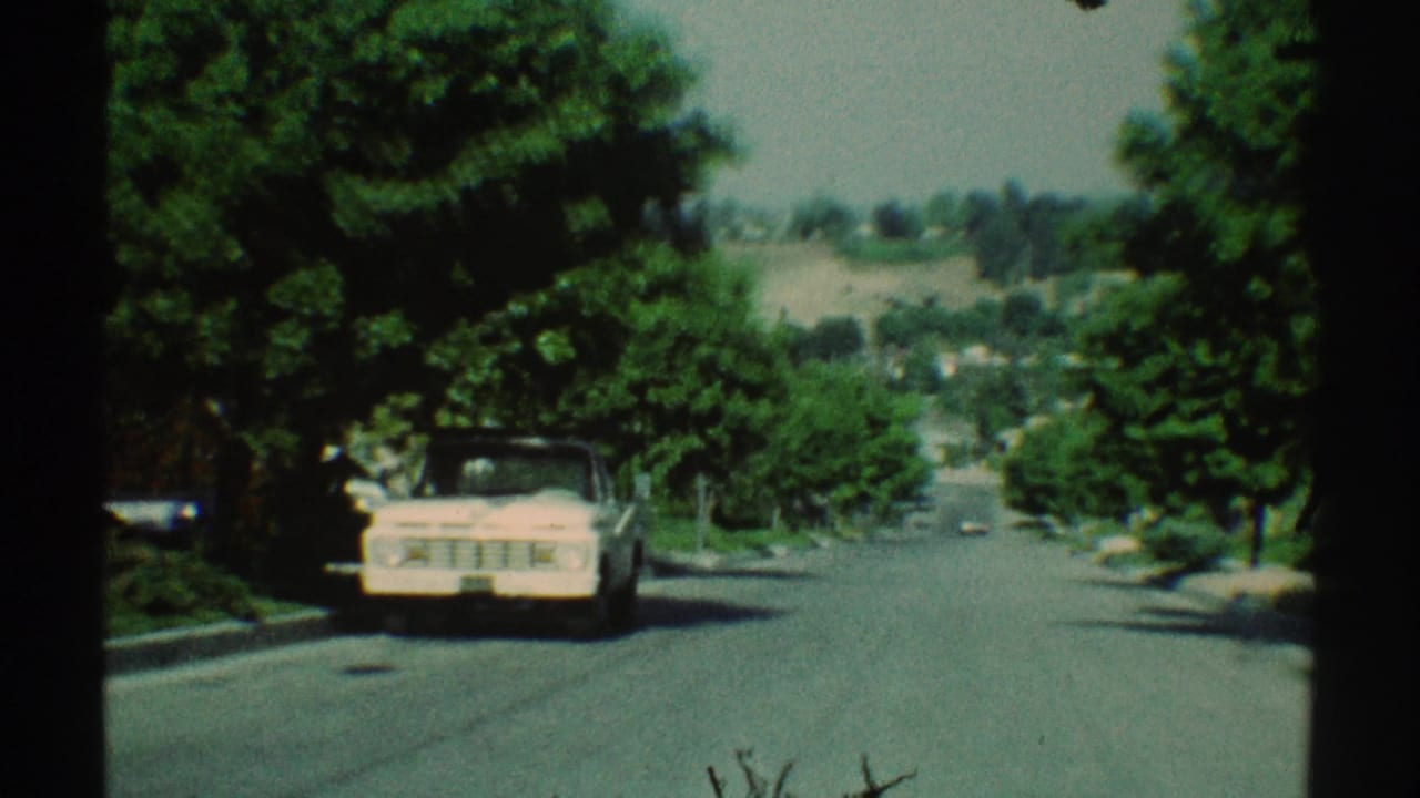 1969 Woodland Hills 8mm frame showing a suburban road, shaded trees, lawns, and a light-colored pickup truck near the left curb.