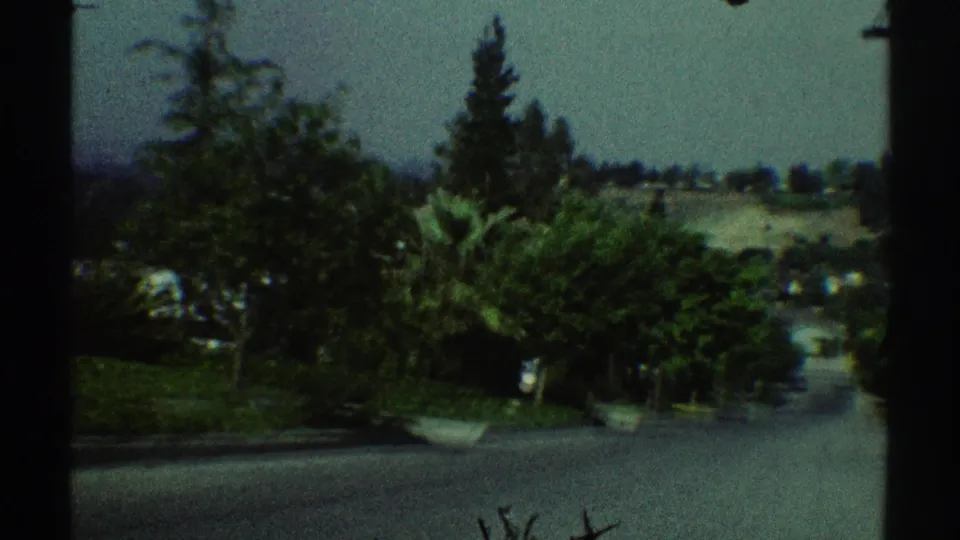 1969 Woodland Hills home-movie frame showing a downhill residential street with trees, lawns, distant hills, and soft 8mm color.