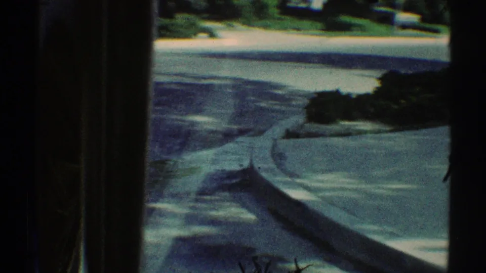 1969 Woodland Hills driving view with curb, street pavement, planted yard edges, and dark 8mm frame borders.
