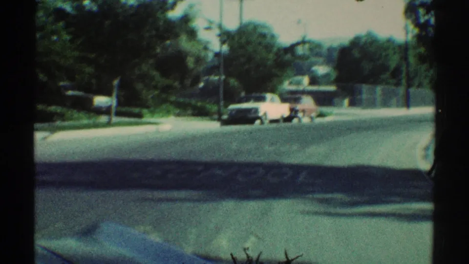 1969 Woodland Hills residential street with a white car near the curb, tree-lined background, fence line, utility poles, and broad pavement.