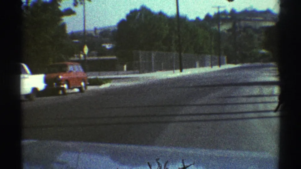 1969 Woodland Hills street view from inside a vehicle, showing older cars, roadside trees, utility poles, and low hills beyond the road.
