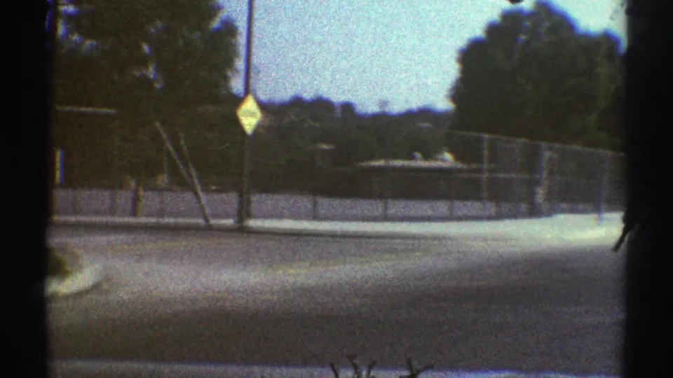 Moving vehicle view in Woodland Hills, California, showing a fenced roadside, sidewalk, signpost, trees, poles, and distant hills.