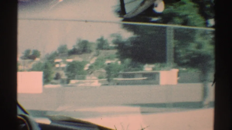 1969 Woodland Hills drive-by view of a quiet fenced school or playground area with trees, low walls, and hazy sunlit pavement.