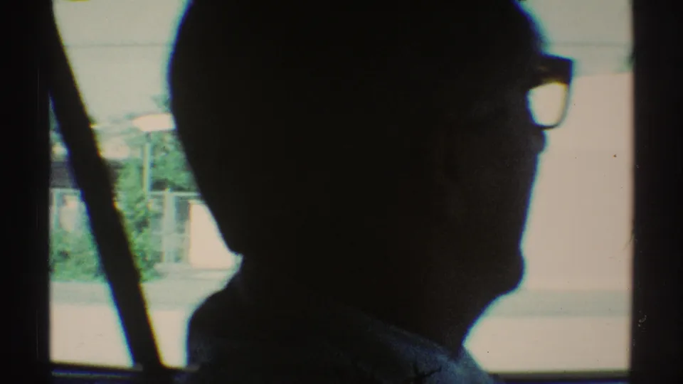 1969 Woodland Hills 8mm frame with the driver in profile silhouette beside a bright window and blurred roadside background.