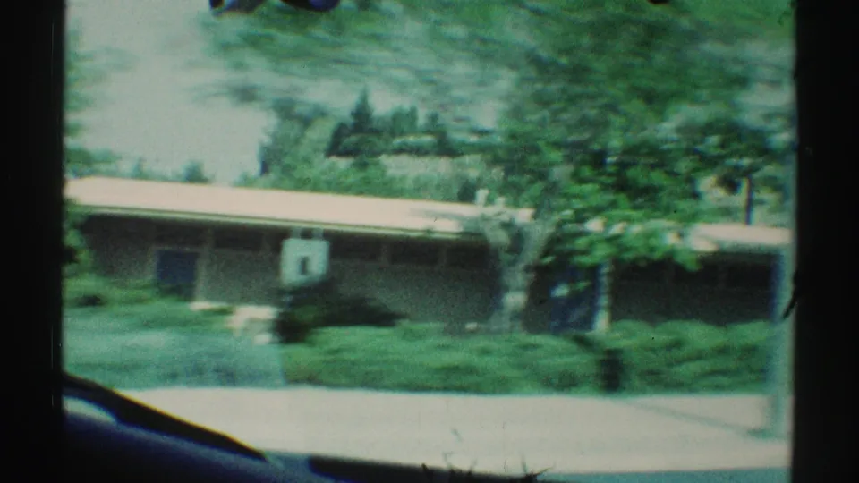 A low Woodland Hills suburban home and landscaped greenery pass outside the car window in soft, color-shifted 8mm footage.