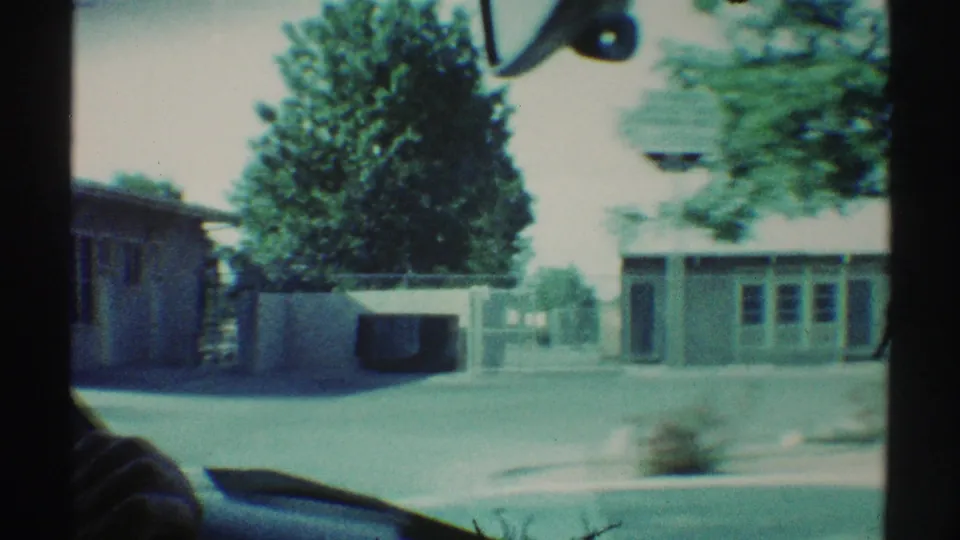 1969 Woodland Hills drive-by frame with a windshield pillar, school buildings, fence, trees, and open pavement.