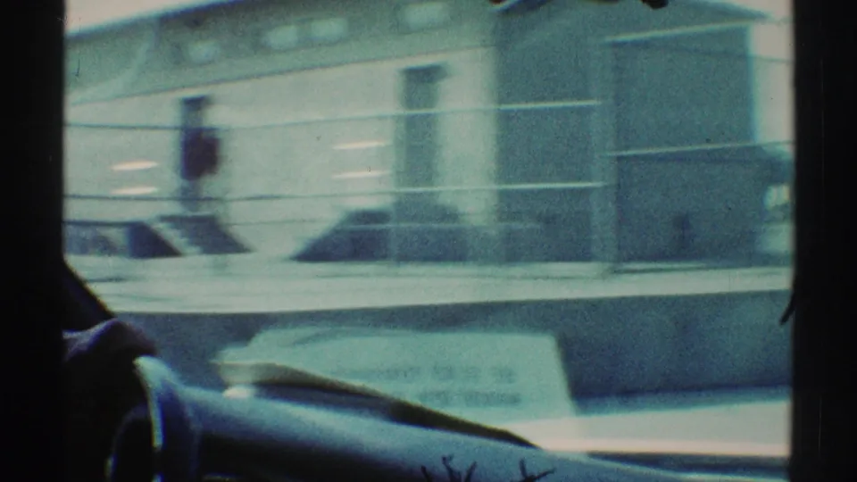 1969 Woodland Hills driving shot with dark windshield framing, dashboard edge, and an industrial-style building passing outside.