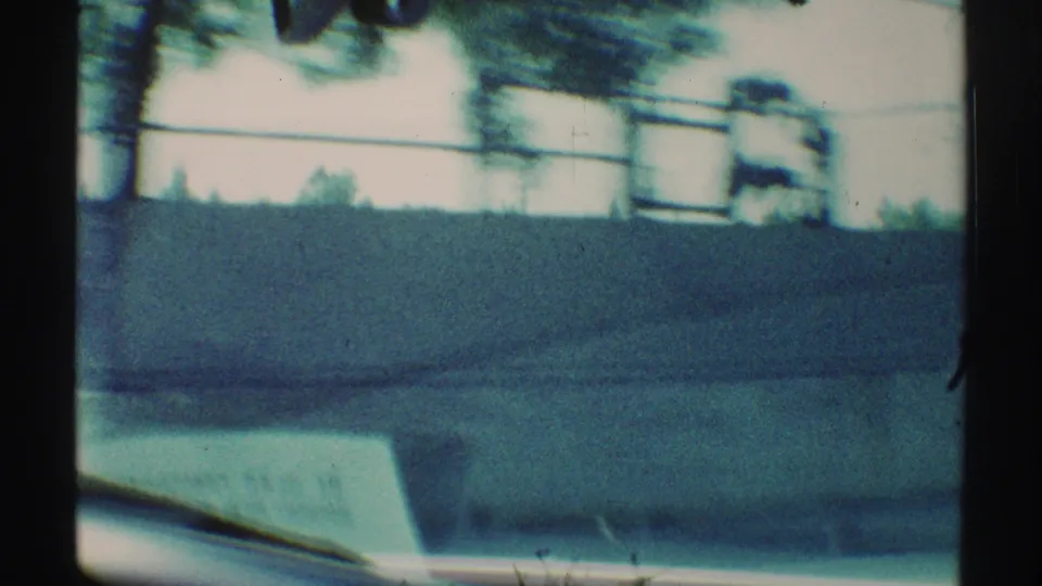 Woodland Hills driving view from 1969, with a low roadside wall, fence, trees, and the lower edge of the car windshield in motion blur.