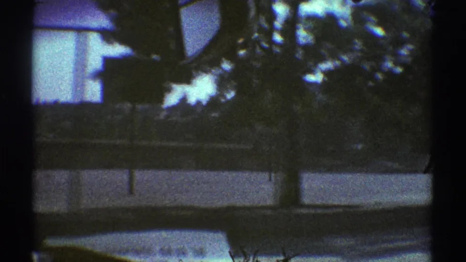 The moving-car view passes trees, a low wall or curb, and a pale suburban building shape in 1969 Woodland Hills footage.