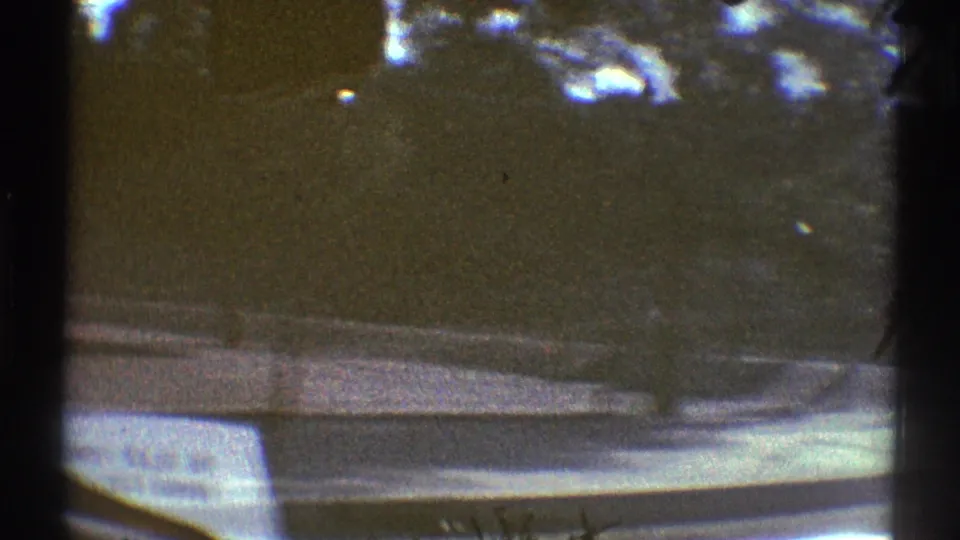 1969 Woodland Hills home-movie view from a car looking along a tree-lined residential street with curb and sidewalk visible.