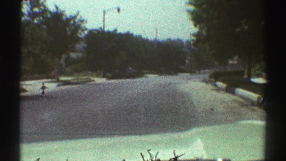 Forward-facing 8mm frame from a car on a Woodland Hills residential street, with trees, a street lamp, and bright pavement ahead.