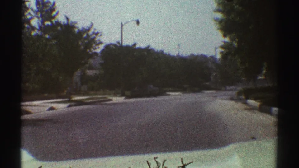 Woodland Hills car POV shows a broad residential street bordered by lawns, trees, sidewalks, and dark film gate edges.