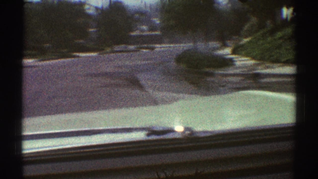 View over a car hood toward a quiet residential street with sidewalks and trees.