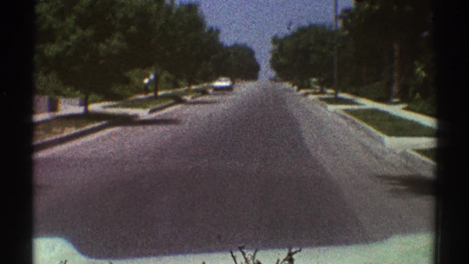 The home-movie camera continues forward along a Woodland Hills residential road bordered by mature trees and sidewalks.