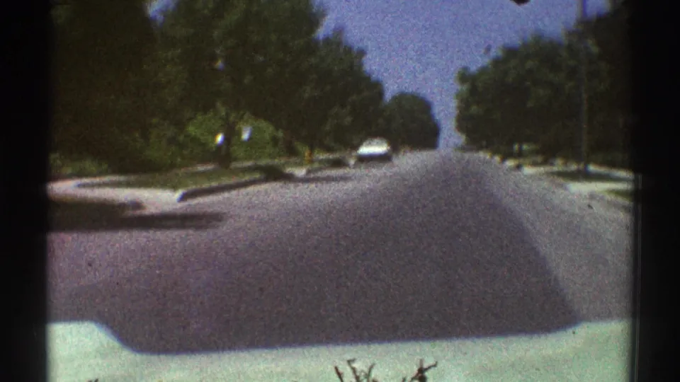 1969 Woodland Hills home-movie frame looking down a quiet tree-lined suburban road from inside or near a moving car.