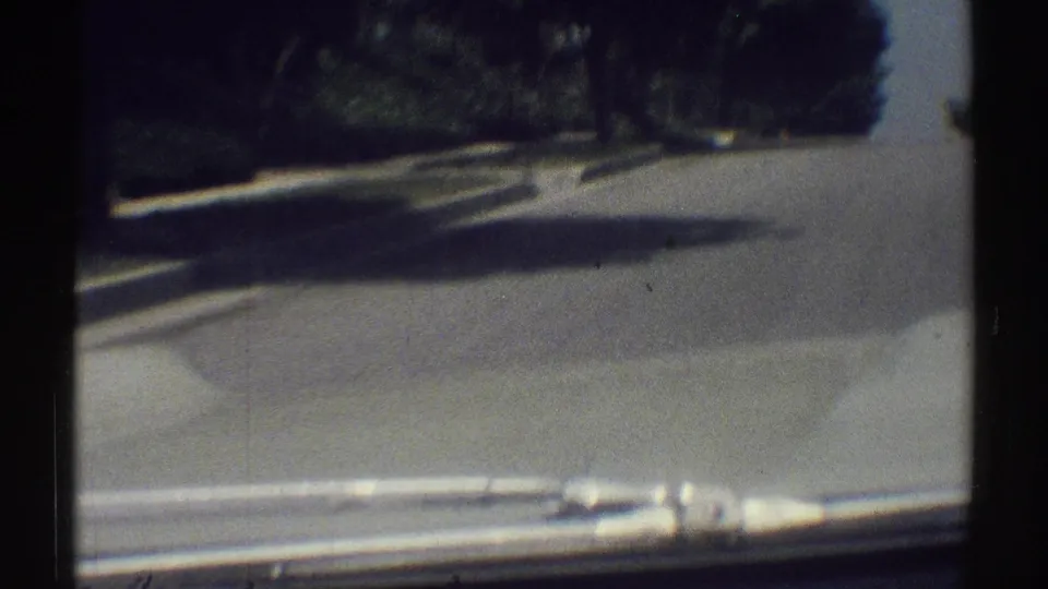 Moving-vehicle view of a Woodland Hills street with windshield edge, curb, trees, and bright pavement.