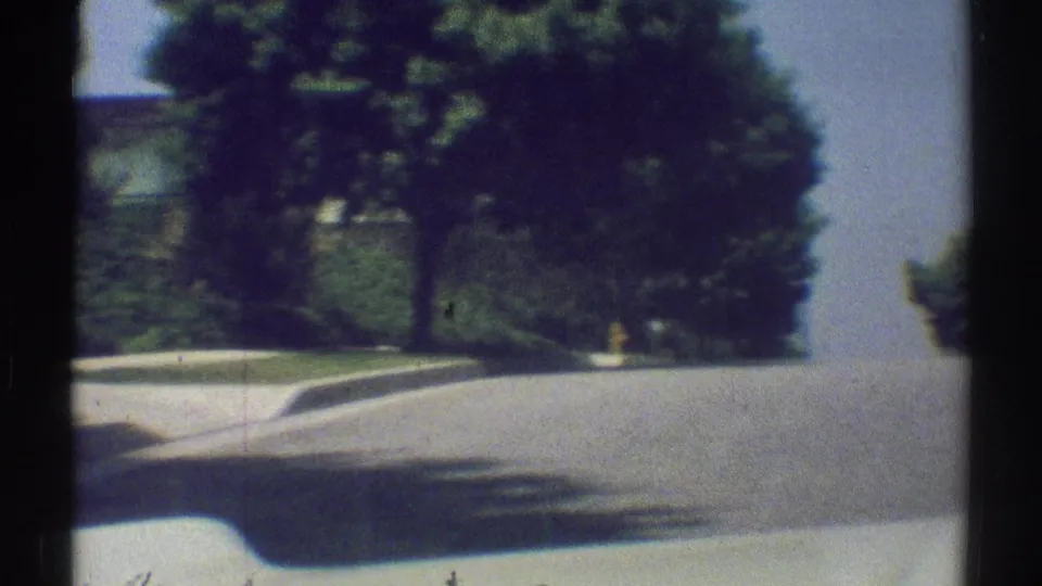 Woodland Hills street view from a moving vehicle in 1969, showing broad pavement, sidewalk, curb, and dense roadside trees.