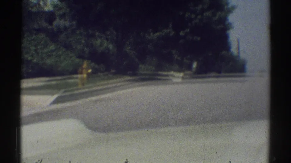 Motion-blurred 1969 Woodland Hills street frame with a yellow hydrant, sidewalk, curb, trees, and shaded pavement.