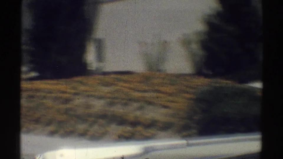 1969 Woodland Hills frame with a soft drive-by view of a white residential wall, lawn, shrubs, and trees.