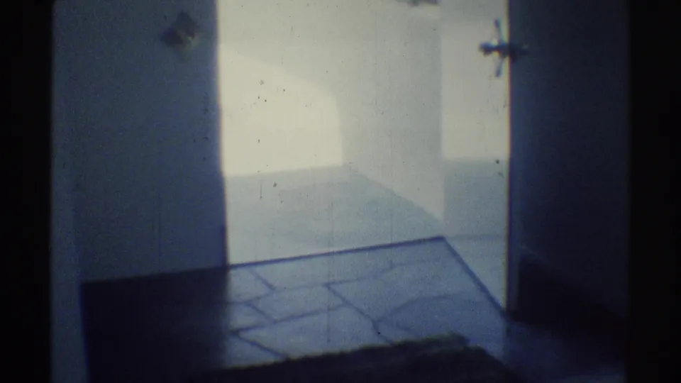 1969 Woodland Hills frame looking into a dim garage or entry area with a paved floor and bright exterior beyond.