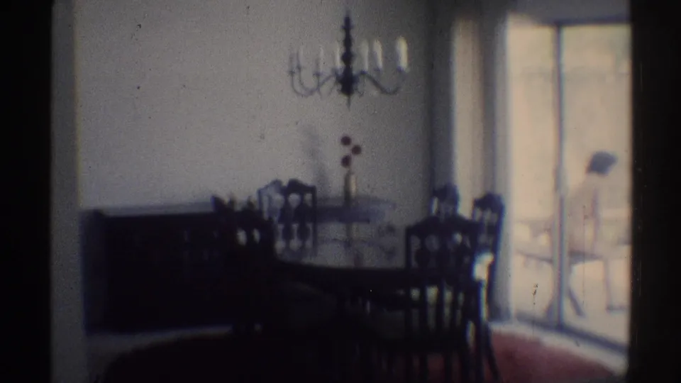 1969 Woodland Hills interior view of a dining set near glass doors, with a person in light clothing seated outside on the patio.