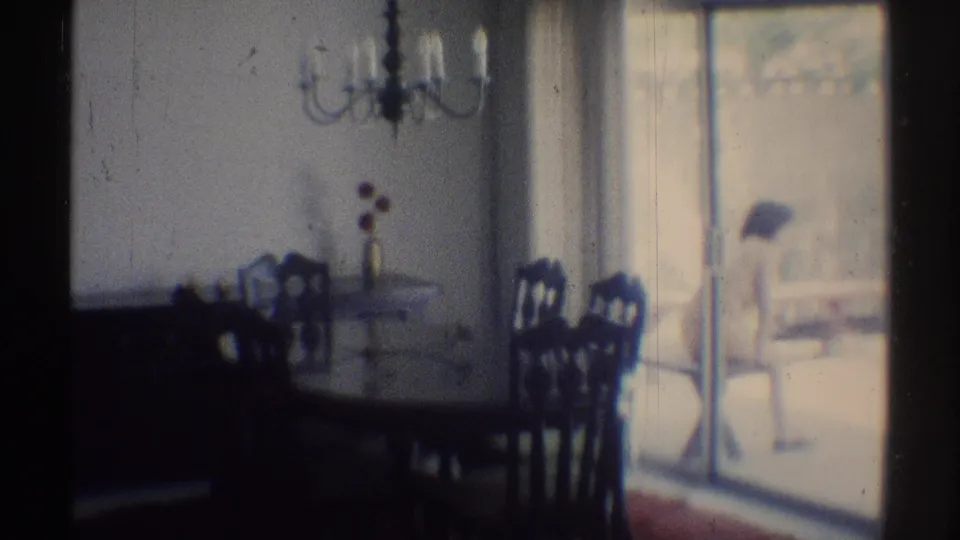 Soft 8mm frame of a Woodland Hills dining room, showing chairs, chandelier, flowers on the table, and bright patio doors.