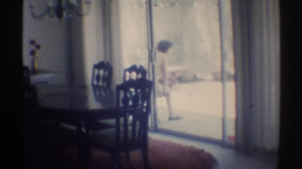 1969 Woodland Hills dining room frame with dark chairs in front and a sunlit patio figure beyond the sliding doors.