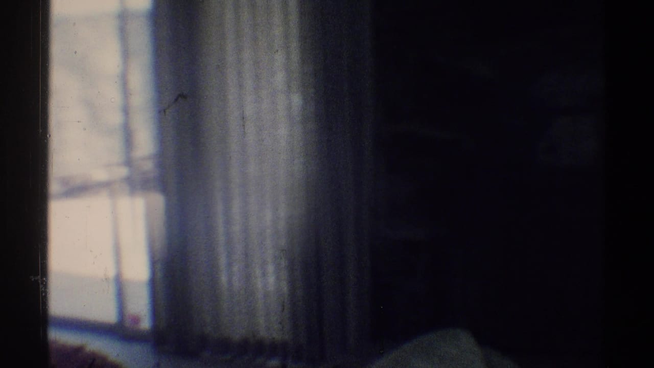 1969 Woodland Hills home-movie frame showing a dim room with a bright window, sheer curtains, and shadowed interior surfaces.