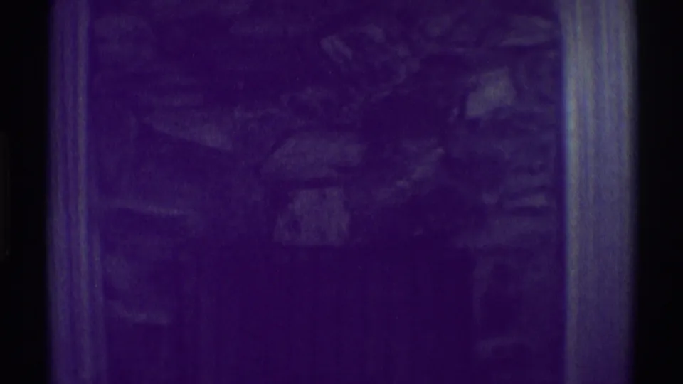1969 Woodland Hills home-movie frame showing a dim stone fireplace wall with framed art and heavy purple color shift.