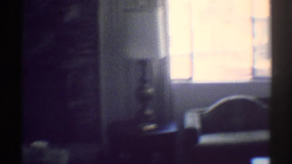 1969 Woodland Hills interior frame with a bright window, lamp on a table, dark fireplace wall, and chair back in soft 8mm focus.
