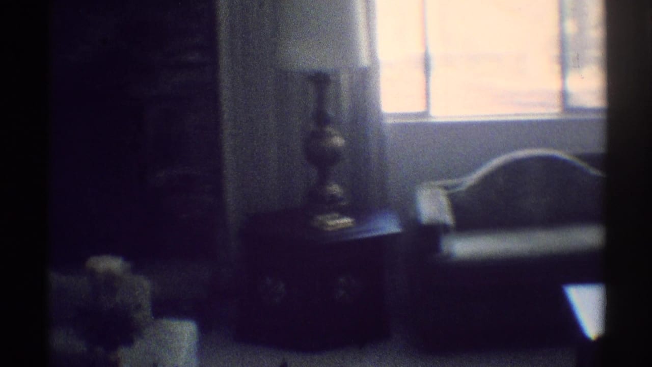 1969 Woodland Hills home interior with a curved-back sofa below bright windows, a side table, and a shaded lamp.