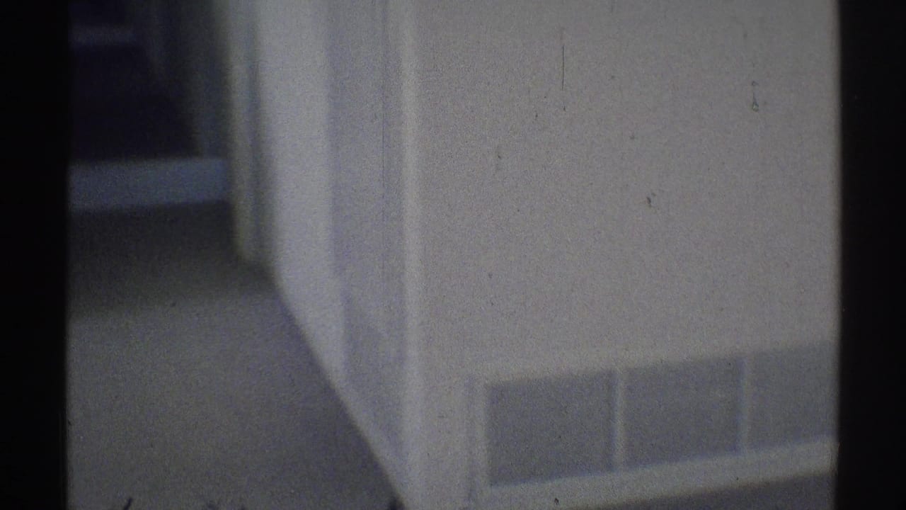 Dim hallway with white wall, carpeted floor, wall vent, and doorway edges.