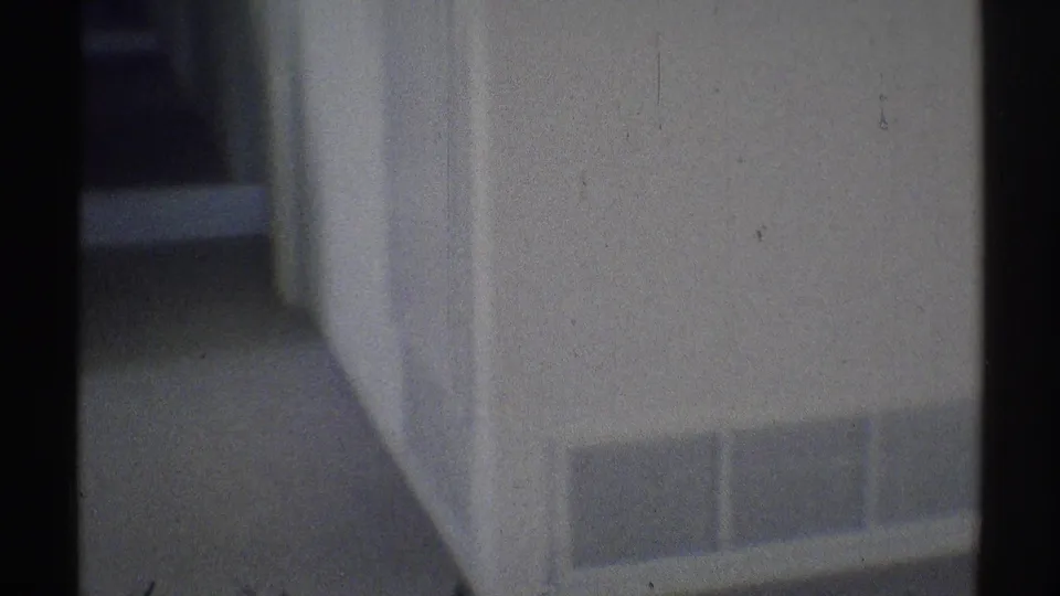1969 Woodland Hills home-movie frame showing a dim residential hallway with white walls, carpet, vent panel, and dark doorframe edges.