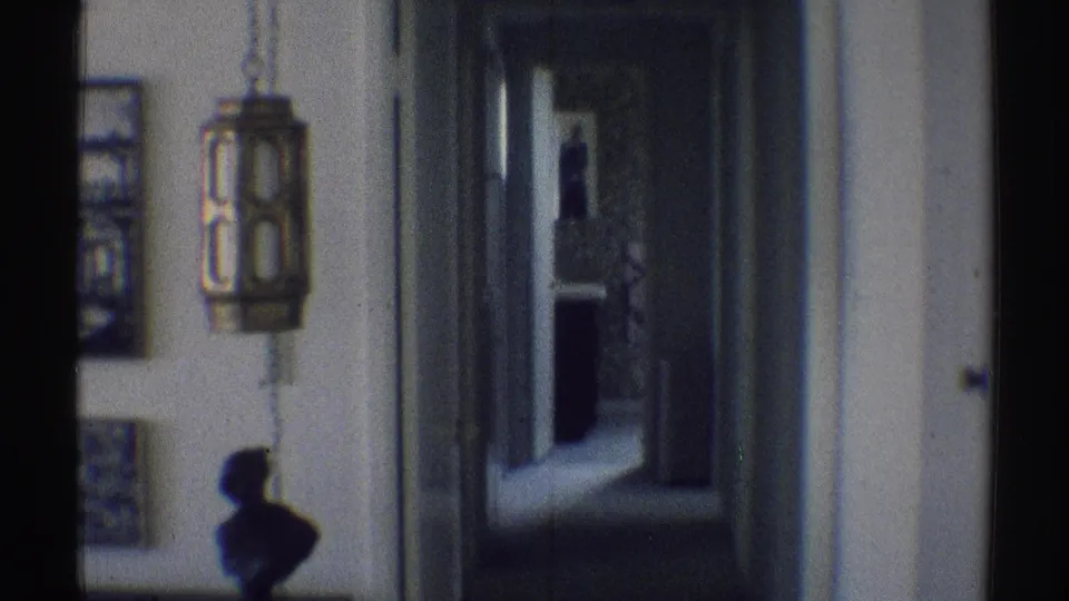 1969 Woodland Hills home interior with a lantern-style wall light, framed pictures, a silhouetted bust, and a corridor leading to an open doorway.