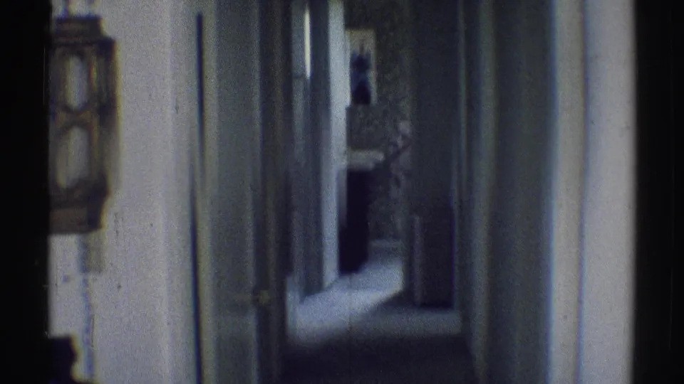 1969 Woodland Hills hallway frame showing a sconce at left, a doorframe and knob at center, and a darker open room beyond the corridor.