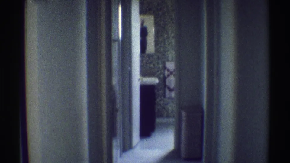 1969 Woodland Hills home interior frame with a closer handheld view down the hallway toward a partially visible person near the doorway.