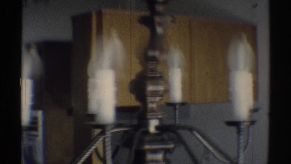 Soft 8mm frame of a chandelier with white candle sleeves, filmed inside a Woodland Hills home interior in 1969.