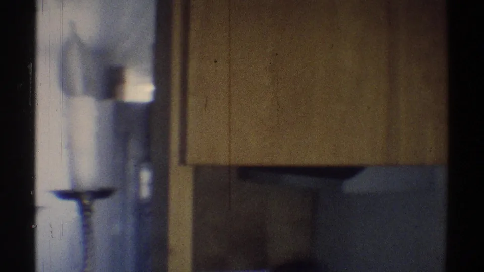 Home-movie frame showing part of the candle-style light fixture near a wall and cabinet in a private California interior.