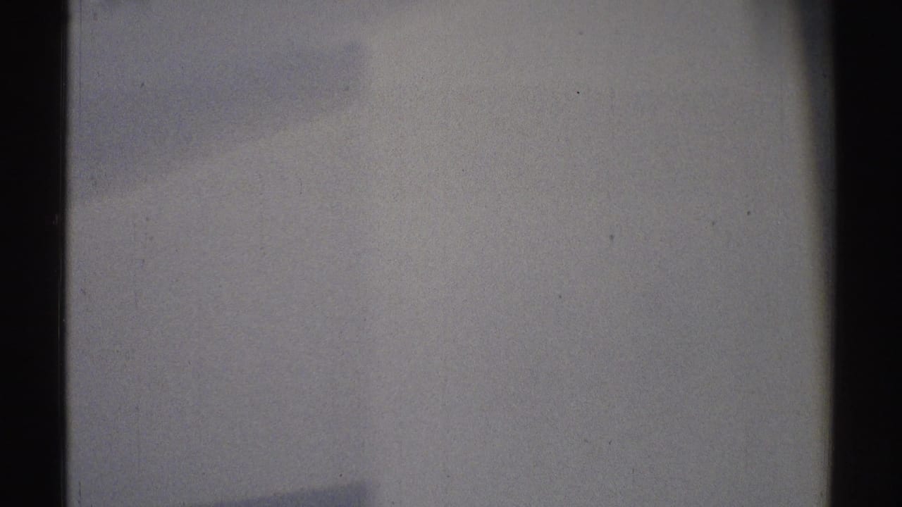 Soft, dim close view of a pale wall with dark vertical edges and film grain.