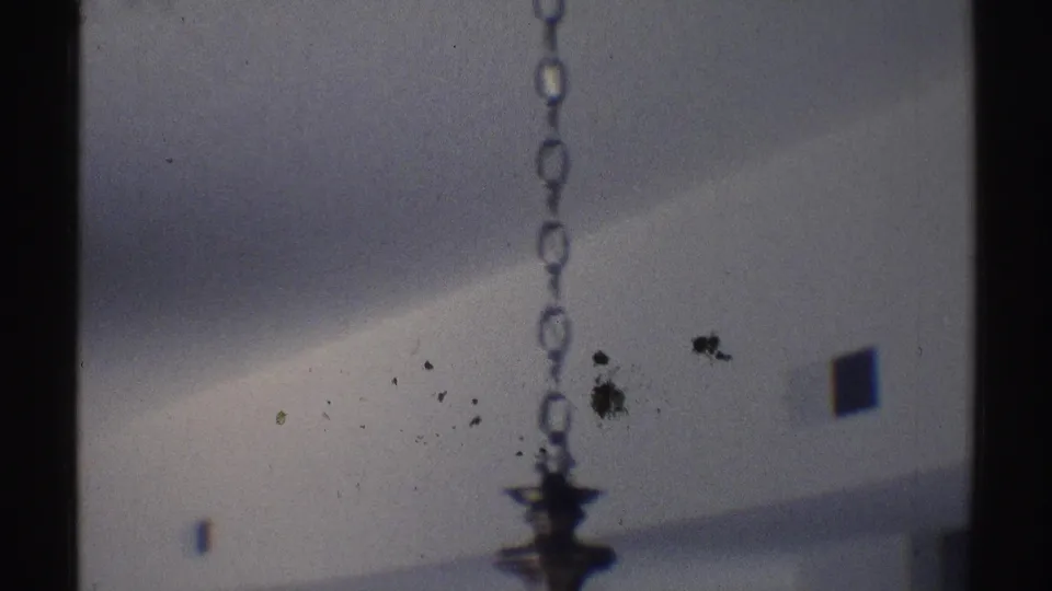Dim Woodland Hills home interior frame with a hanging chain, ceiling shadow, and dark vertical divider on 8mm film.