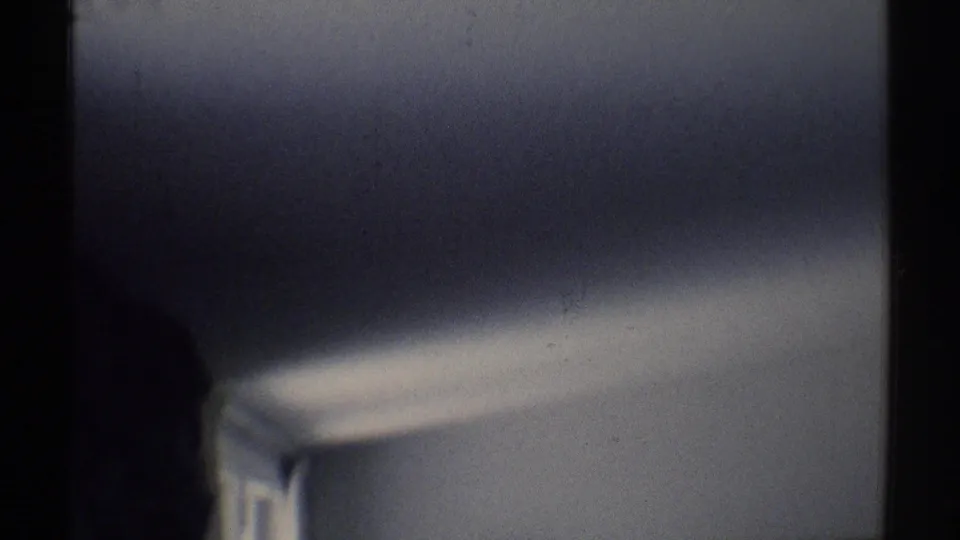 Soft 1969 home-movie frame showing a pale wall, ceiling curve, and dark divider inside a private Woodland Hills room.