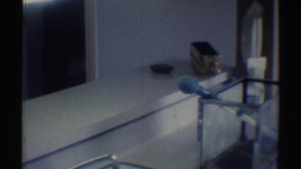 1969 Woodland Hills home-movie frame showing a dim bathroom counter, mirror edge, toiletries, and a blue grooming item.