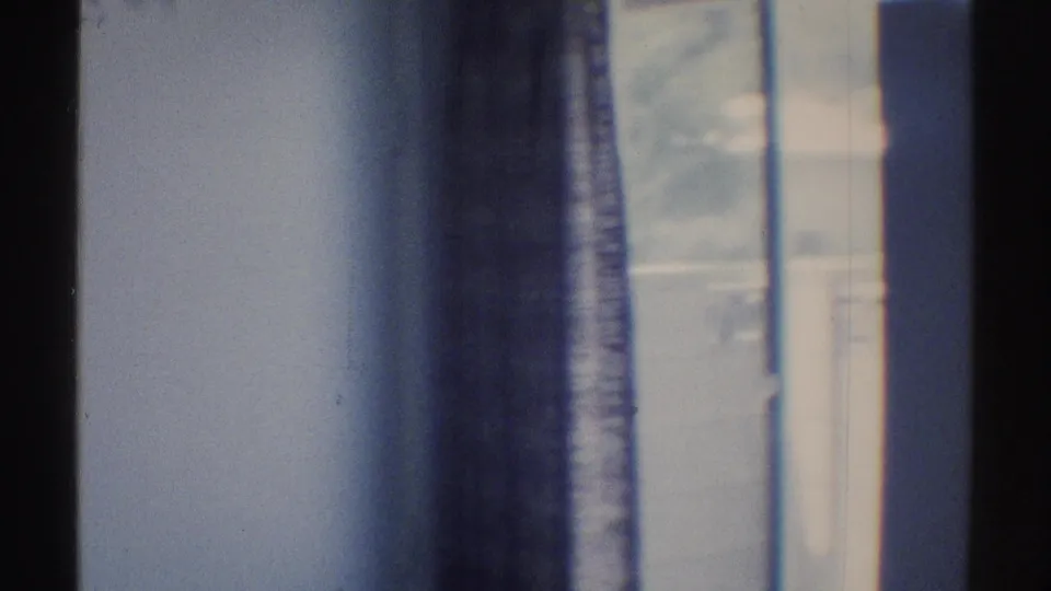 Soft, blue-tinted 8mm frame of an interior wall flanked by dark window or curtain edges in the Woodland Hills room.
