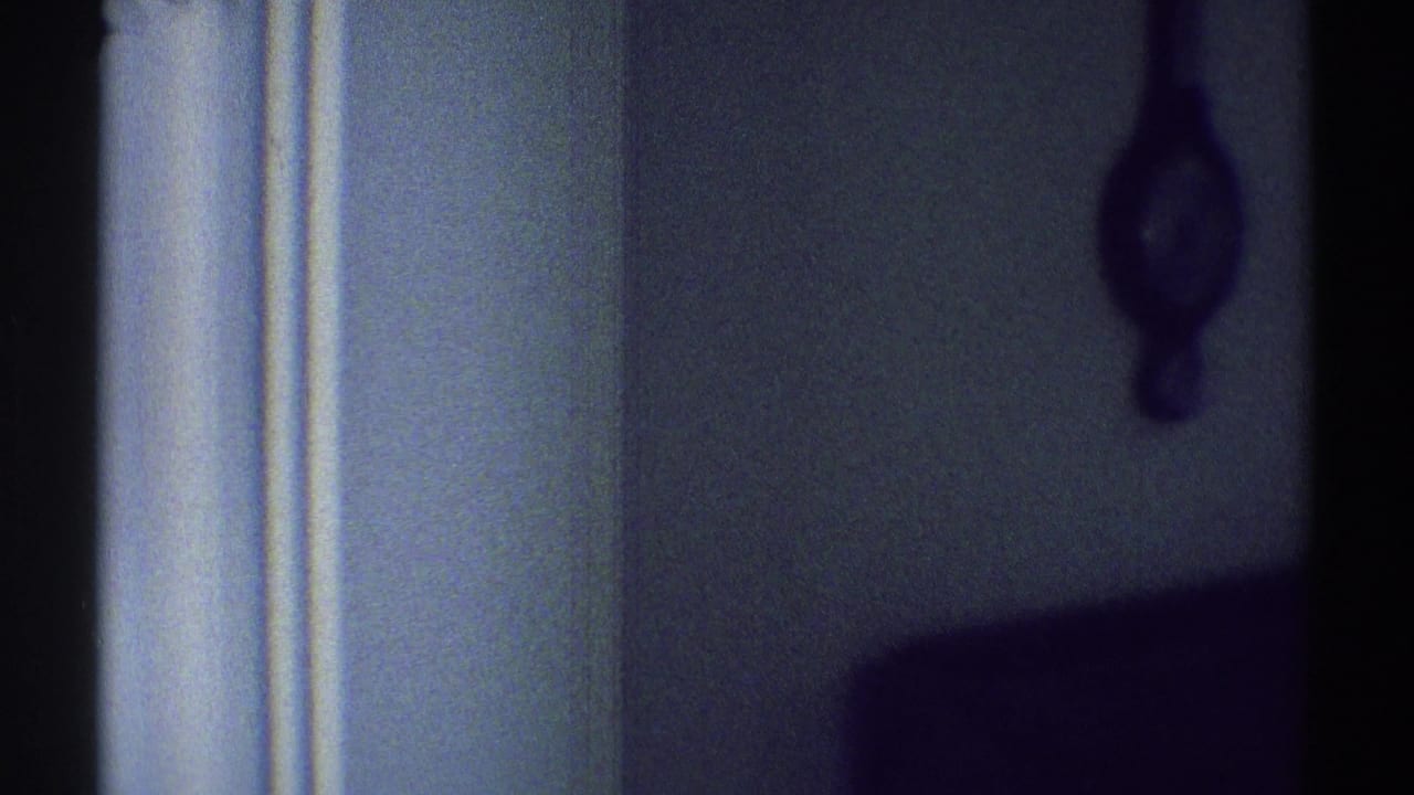 1969 Woodland Hills home-movie frame showing a dim wall, brown hanging clock, and white interior trim in soft 8mm focus.