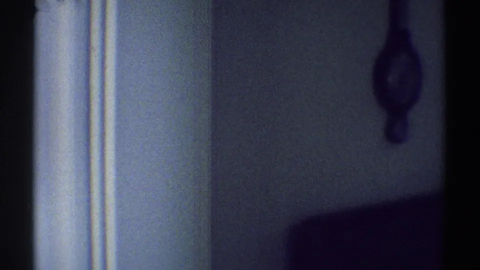 1969 Woodland Hills home-movie frame showing a dim wall, brown hanging clock, and white interior trim in soft 8mm focus.