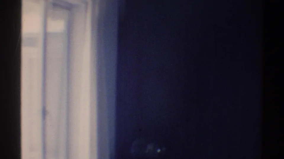 A late clip frame from the 1969 Woodland Hills interior, with an open window, white trim, pale curtain, and dark foreground area.