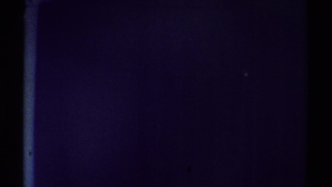 1969 Woodland Hills home-movie frame showing a dim interior surface, heavy purple shadow, and a slim bright vertical edge.